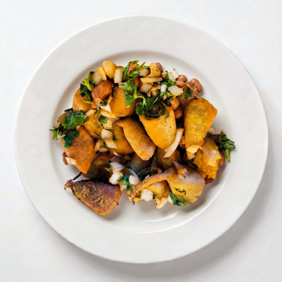 A white plate holds a dish of fried plantains, chickpeas, onions, and cilantro.