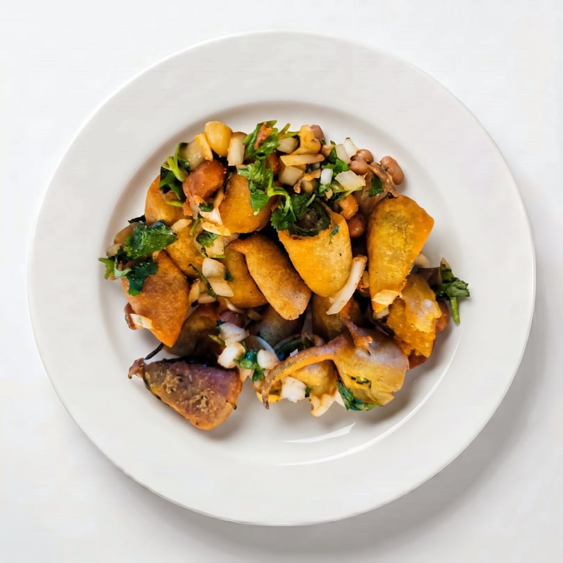 A white plate holds a dish of fried plantains, chickpeas, onions, and cilantro.