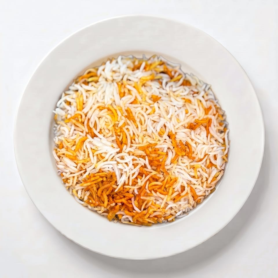 Overhead view of a white plate filled with fluffy white and orange biryani rice.